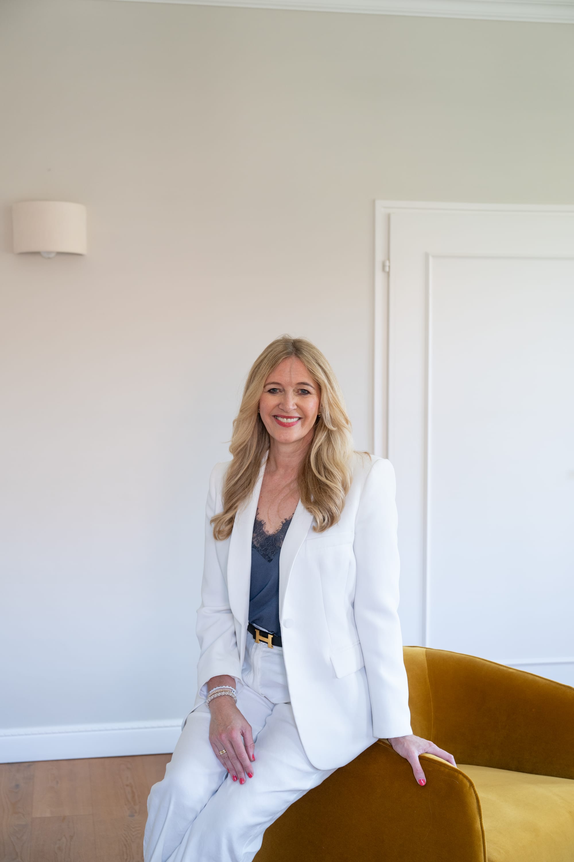 Heike Ewald, Inhaberin von EWALD Real Estate, in hellem Anzug auf einer Sessellehne sitzend