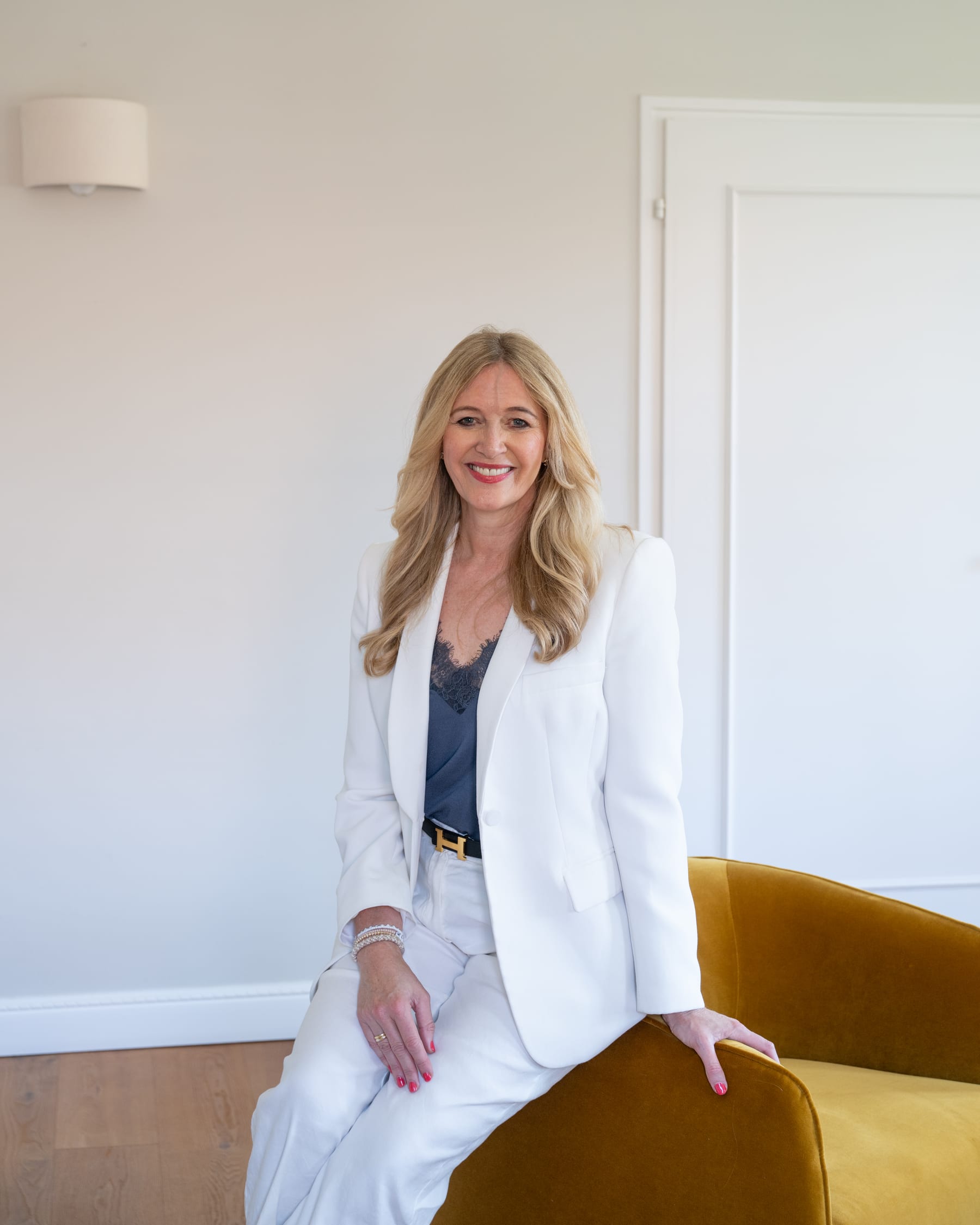 Heike Ewald, Inhaberin von EWALD Real Estate, in hellem Anzug auf einer Sessellehne sitzend